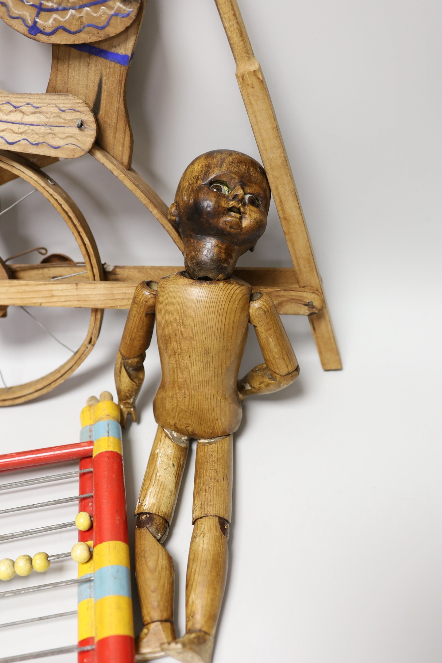 A Victorian carved pine jointed peg doll, jointed wood uni-cyclist toy, two abacuses and an early 20th century German tin plate and clockwork jockey on racehorse